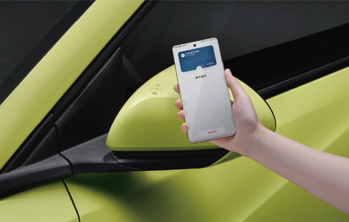 A hand holding a smartphone displaying a control interface for the BYD Seagull vehicle, with a close-up of the car's side mirror and vibrant green body color.
